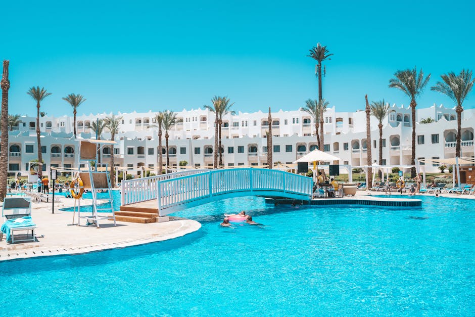 Scenic view of a resort pool with a footbridge and palm trees under a clear sky.