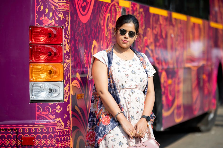 A stylish woman in sunglasses poses by a vibrantly decorated bus on a sunny day.