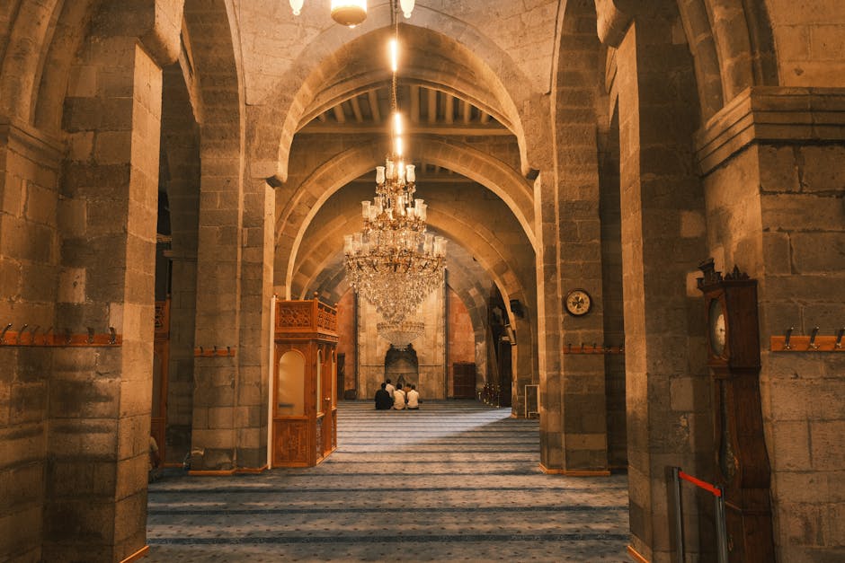 A stunning view of a grand mosque interior featuring a beautiful chandelier and worshippers in prayer.